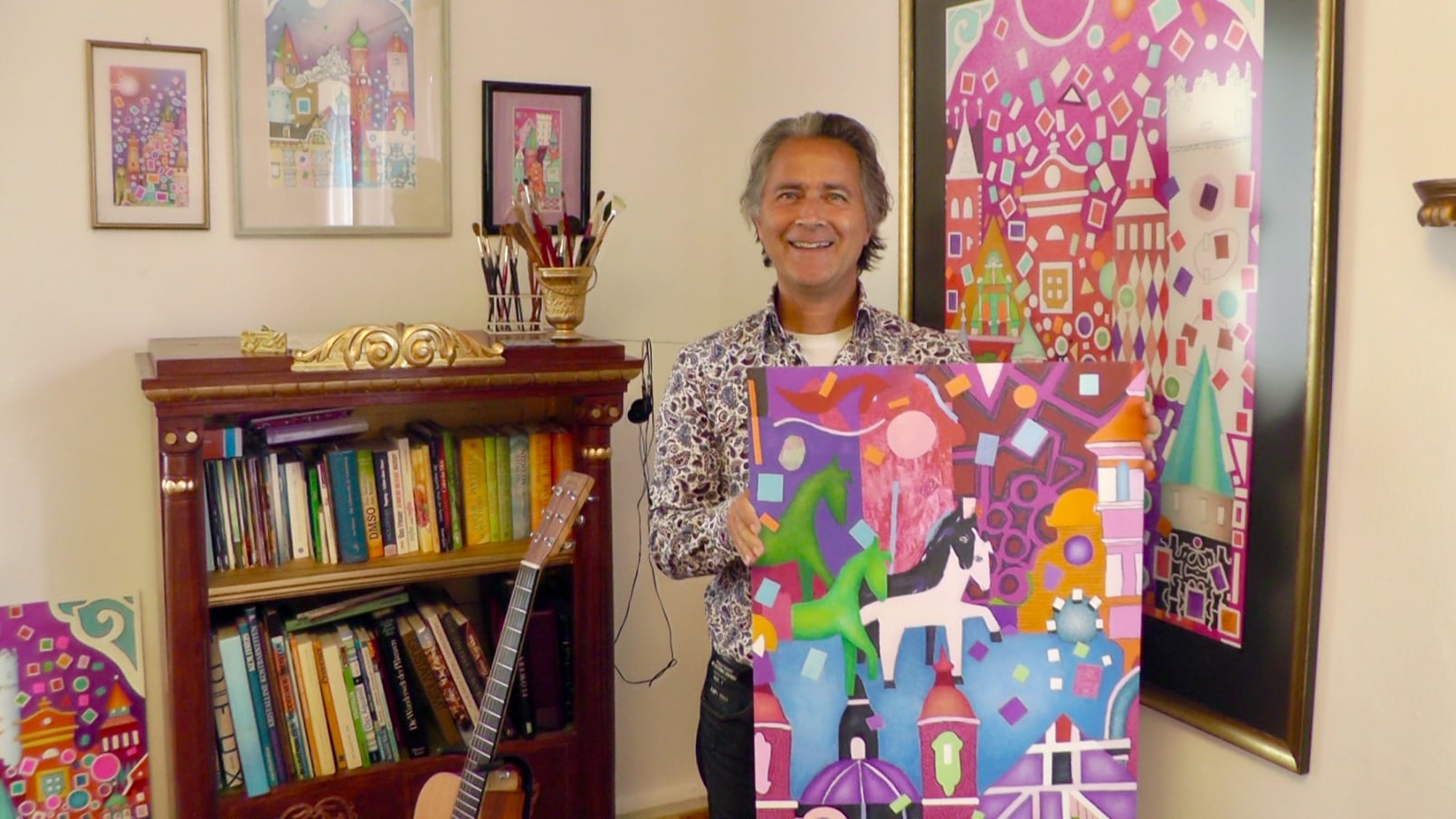 Stefan Eichler in seinem Atelier mit einem Gemälde in den Händen, umgeben von eigenen Bildern